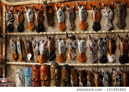 Unique wooden zebra masks displayed on a wall in a craft market during the daytime in a vibrant cultural setting Unique wooden zebra masks displayed on a wall in a craft market during the daytime in a vibrant cultural setting 141485868