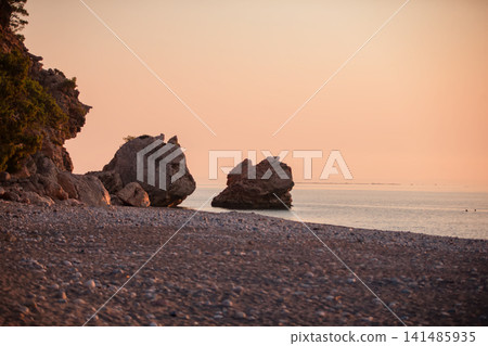 Sunset over the tranquil beach with distinct rock formations along the shoreline Sunset over the tranquil beach with distinct rock formations along the shoreline 141485935