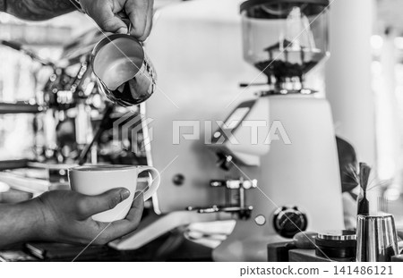 Barista making a Cappuccino coffee in modern coffeeshop with professional equipment BW Black and White stock photo Barista making a Cappuccino coffee in modern coffeeshop with professional equipment BW Black and White stock photo 141486121