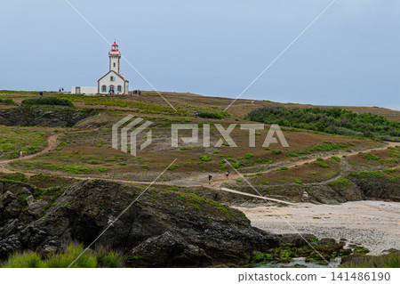 Solitary White Lighthouse on Rugged Coastal Cliffs Overlooking Rocky Beach and Rolling Moorland 141486190