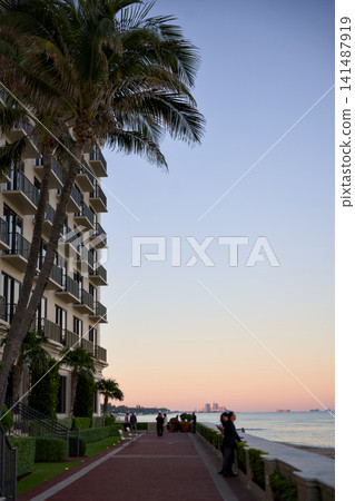 Oceanfront Promenade Beside A Palm Tree And Condo Building At Dusk Oceanfront Promenade Beside A Palm Tree And Condo Building At Dusk 141487919