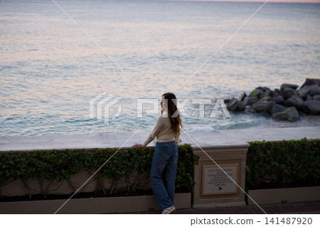 Woman Standing By The Sea Wall In A Wide Coastal Landscape Woman Standing By The Sea Wall In A Wide Coastal Landscape 141487920