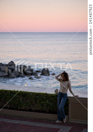 Woman Gazes At The Sea While Standing Along A Coastal Wall 141487923