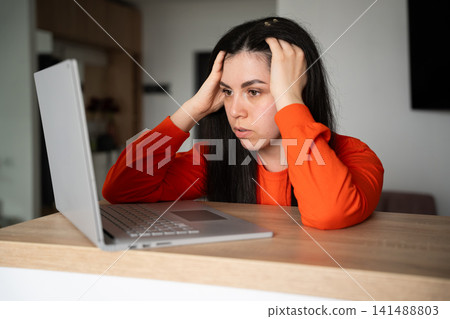 Frustrated young woman holding her head while looking at a laptop screen indoors. Stress management digital burnout and workplace challenges Frustrated young woman holding her head while looking at a laptop screen indoors. Stress management digital burnout and workplace challenges 141488803