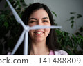 Smiling woman holding a small wind turbine model indoors. Renewable energy advocacy and eco-friendly STEM initiatives 141488809