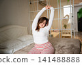 Woman stretching on bed in cozy bedroom during morning routine. Wellness and healthy wake-up habits for improved sleep quality 141488888