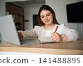 Young woman writing in notebook while using laptop at home workspace. Remote work and online learning productivity and freelance note-taking 141488895