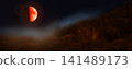 Blood moon with orange surface over forest at night. Half of the moon is illuminated. 141489173