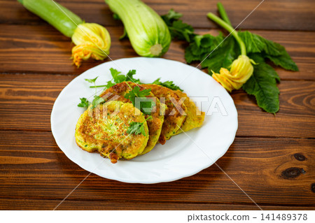Fresh vegetable zucchini pancakes on white plate with rustic wooden background Fresh vegetable zucchini pancakes on white plate with rustic wooden background 141489378