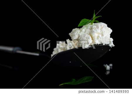 Fresh cottage cheese with green basil on black reflective background Fresh cottage cheese with green basil on black reflective background 141489393