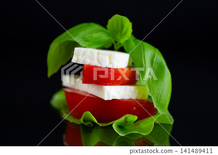 Fresh Mediterranean cheese with basil leaves on elegant black background Fresh Mediterranean cheese with basil leaves on elegant black background 141489411