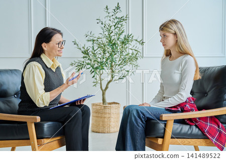 Friendly female psychologist smiling and supporting teenage girl at therapy Friendly female psychologist smiling and supporting teenage girl at therapy 141489522
