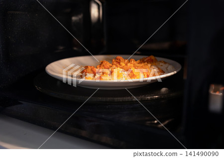 Plate with food heating inside a microwave oven, capturing a simple everyday meal preparation scene in a home kitchen with warm interior lighting and practical domestic use 141490090