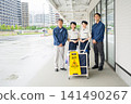 Four cleaning staff members, two men and one woman, lined up in front of the cleaning cart. 141490267