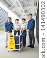 Four cleaning staff members, two men and one woman, lined up in front of the cleaning cart. 141490302