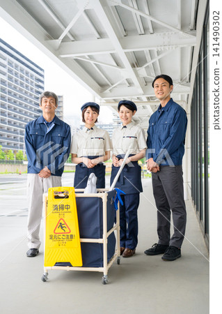 Four cleaning staff members, two men and one woman, lined up in front of the cleaning cart. Four cleaning staff members, two men and one woman, lined up in front of the cleaning cart. 141490302