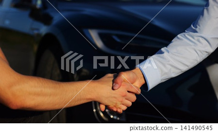 Male hand giving key of car to buyer of electric automobile outdoor. Handshake between salesman and new owner of modern auto after successful deal. Concept of buy or rent car. Slow mo Male hand giving key of car to buyer of electric automobile outdoor. Handshake between salesman and new owner of modern auto after successful deal. Concept of buy or rent car. Slow mo 141490545