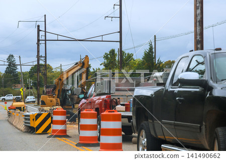 Construction work occurs on road with heavy equipment traffic cones cars are waiting due to delays. Construction work occurs on road with heavy equipment traffic cones cars are waiting due to delays. 141490662