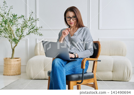 Mature confident female specialist sitting in chair with laptop in home office 141490694