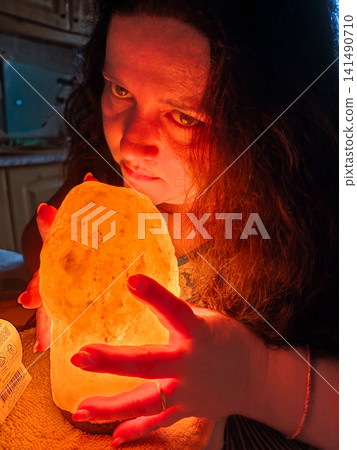 Woman holding glowing himalayan salt lamp in dark room Woman holding glowing himalayan salt lamp in dark room 141490710