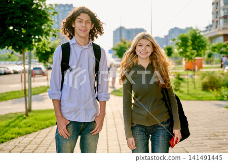 Two happy diverse teenager students with backpacks standing outside on a sunny city street Two happy diverse teenager students with backpacks standing outside on a sunny city street 141491445