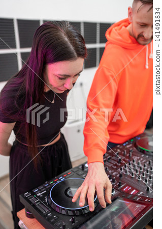 DJ teaches music mixing on professional equipment with young woman in recording studio. DJ, music mixing, studio, equipment, teaching 141491834