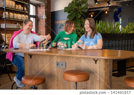 Colleagues or friends taking notes and collaborating at a stylish cafe counter in green setting. Collaboration, notes, cafe, counter, green. Colleagues or friends taking notes and collaborating at a stylish cafe counter in green setting. Collaboration, notes, cafe, counter, green. 141491857