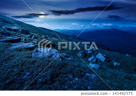 mountain landscape with grass and rock on a slope at night. mysterious view in to the distant valley of carpathian mountains. full moon over mountainous fantasy scenery of ukraine in summer mountain landscape with grass and rock on a slope at night. mysterious view in to the distant valley of carpathian mountains. full moon over mountainous fantasy scenery of ukraine in summer 141492575