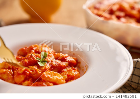 Gnocchi in tomato sauce served on plate with basil garnish and fork Gnocchi in tomato sauce served on plate with basil garnish and fork 141492591