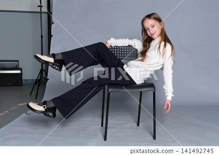 Girl sits wooden step stool with hands gently placed on her knee, subtle smile and quiet confidence Girl sits wooden step stool with hands gently placed on her knee, subtle smile and quiet confidence 141492745