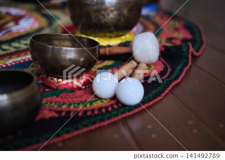 Detailed view of singing bowls and soft sound bath mallets placed on an ornate textile rug in a cozy studio. Mindfulness, resonance, and gentle rhythms support relaxation and inner balance. Detailed view of singing bowls and soft sound bath mallets placed on an ornate textile rug in a cozy studio. Mindfulness, resonance, and gentle rhythms support relaxation and inner balance. 141492789