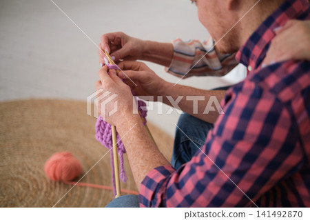 homely setting featuring tender teaching moment. mother instructs her adult son in knitting techniques during his visit, fostering special bond over an unexpected activity. simple pleasures of life 141492870