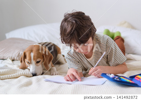 serene scene boy immersed in his drawing while his furry friend relaxes nearby, demonstrating how artistic expression and a calming environment can work together to promote mindfulness in children. serene scene boy immersed in his drawing while his furry friend relaxes nearby, demonstrating how artistic expression and a calming environment can work together to promote mindfulness in children. 141492872