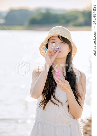 夏天,一位戴著草帽的女子在水邊吹肥皂泡。 夏天,一位戴著草帽的女子在水邊吹肥皂泡。 141494852
