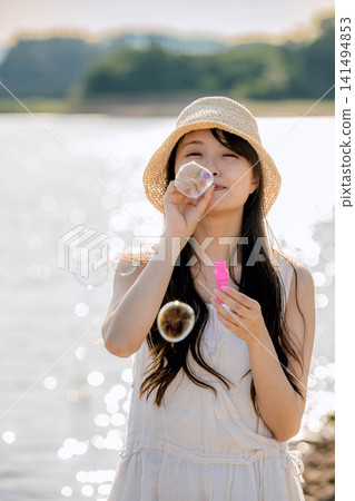 一位女士在波光粼粼的水面上吹肥皂泡。 一位女士在波光粼粼的水面上吹肥皂泡。 141494853