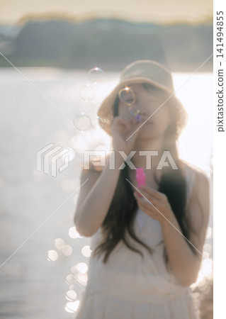 一位戴著草帽的女子對著背光吹肥皂泡。 一位戴著草帽的女子對著背光吹肥皂泡。 141494855