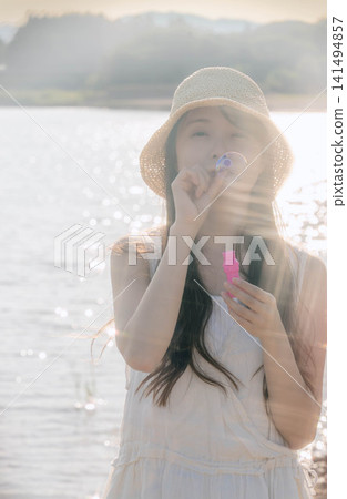 一位身穿白色洋裝的女子在夢幻般的燈光下吹著肥皂泡。 一位身穿白色洋裝的女子在夢幻般的燈光下吹著肥皂泡。 141494857