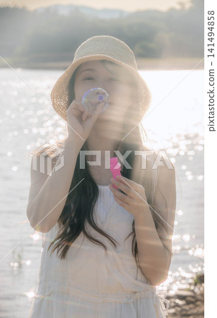 一位戴著草帽的女子在湖邊吹肥皂泡。 一位戴著草帽的女子在湖邊吹肥皂泡。 141494858