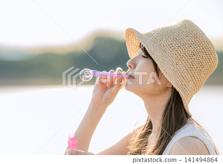 一位身穿白色洋裝的女子正在吹肥皂泡,肥皂泡在逆光下閃閃發光。 一位身穿白色洋裝的女子正在吹肥皂泡,肥皂泡在逆光下閃閃發光。 141494864