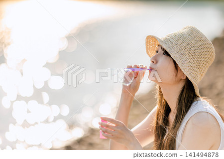 一位戴著草帽的女子正在吹肥皂泡,肥皂泡在逆光下閃閃發光。 一位戴著草帽的女子正在吹肥皂泡,肥皂泡在逆光下閃閃發光。 141494878