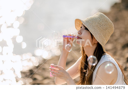 一位身穿白色洋裝的女子在湖邊吹肥皂泡。 一位身穿白色洋裝的女子在湖邊吹肥皂泡。 141494879