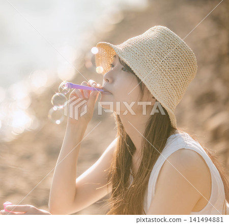 一位女子對著燈光吹肥皂泡,鏡頭捕捉到她的側臉。 一位女子對著燈光吹肥皂泡,鏡頭捕捉到她的側臉。 141494881