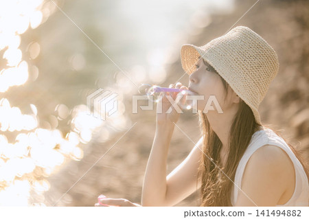 一位身穿白色洋裝的女子在波光粼粼的水面上吹肥皂泡。 一位身穿白色洋裝的女子在波光粼粼的水面上吹肥皂泡。 141494882