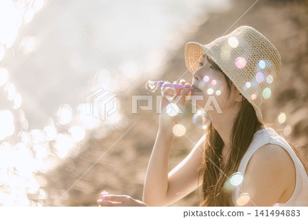 一位戴著草帽的女子在夢幻般的燈光下吹著肥皂泡。 141494883