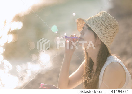 一位身穿白色洋裝的女子正在吹肥皂泡,肥皂泡在逆光下閃閃發光。 一位身穿白色洋裝的女子正在吹肥皂泡,肥皂泡在逆光下閃閃發光。 141494885
