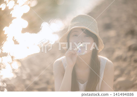 一位戴著草帽的女子在光線充足的環境中吹肥皂泡。 一位戴著草帽的女子在光線充足的環境中吹肥皂泡。 141494886