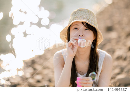 一位戴著草帽的女子在湖邊吹肥皂泡。 一位戴著草帽的女子在湖邊吹肥皂泡。 141494887