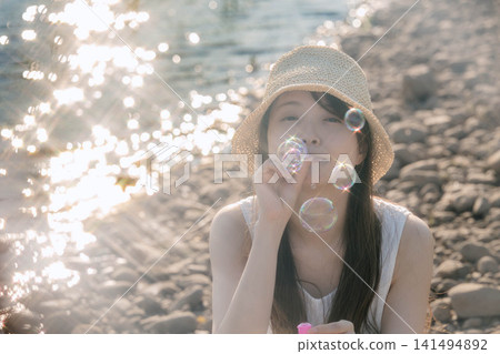 一位女士吹著肥皂泡,在逆光下閃閃發光。 一位女士吹著肥皂泡,在逆光下閃閃發光。 141494892