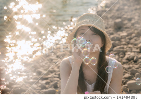 夏天,一位戴著草帽的女子在水邊吹肥皂泡。 夏天,一位戴著草帽的女子在水邊吹肥皂泡。 141494893