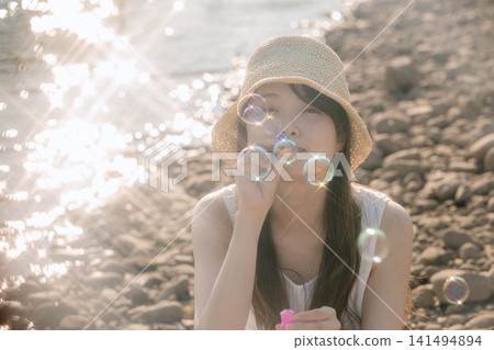 一位女子在陽光普照的湖邊吹肥皂泡。 一位女子在陽光普照的湖邊吹肥皂泡。 141494894